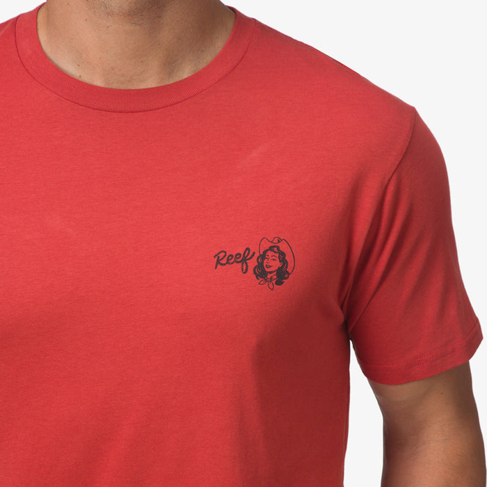 Close-up of the chest area of the red Cowmaid Tee showing the small black Reef logo for menโs beach-inspired apparel.