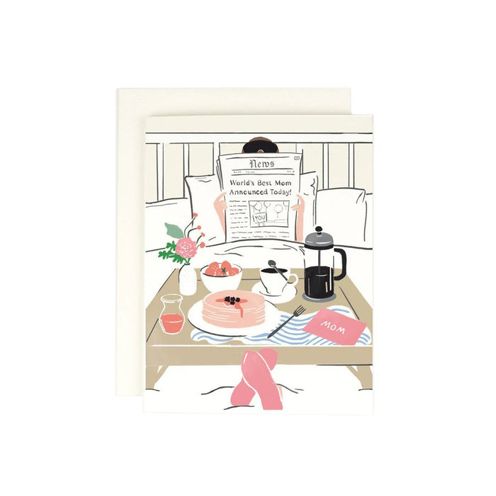 A greeting card depicting a cartoon of a newspaper with the headline 'World's Best Mom Announced Today', presented on a table with breakfast items and a pot of coffee.