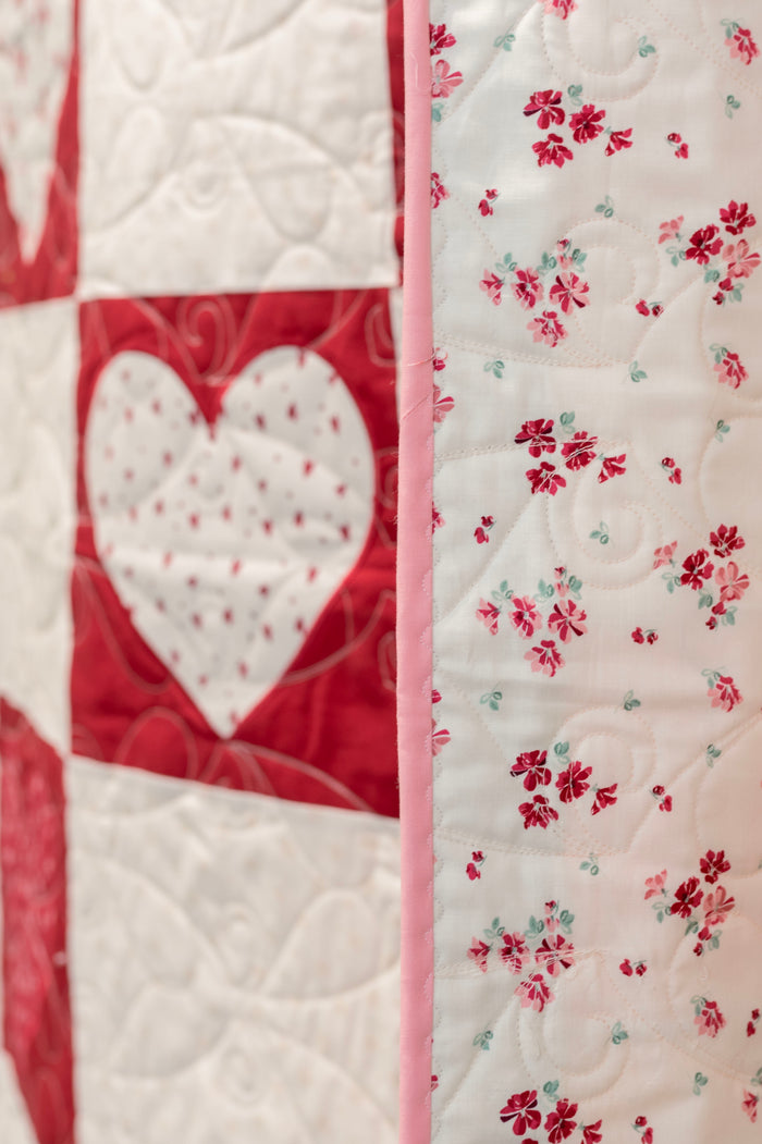 Quilt with heart and floral patterns in red, white, and pink.