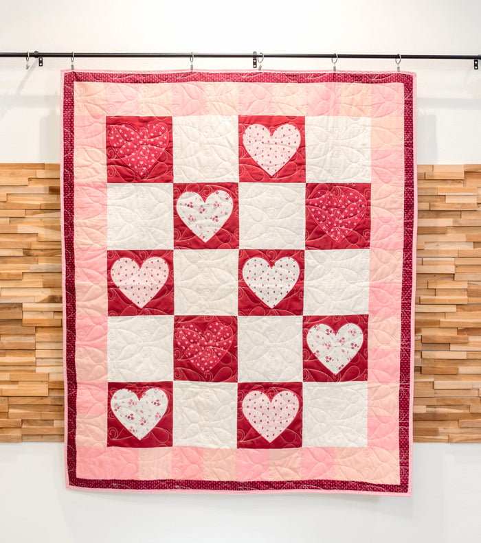 Quilt with heart pattern hanging against a wooden panel background