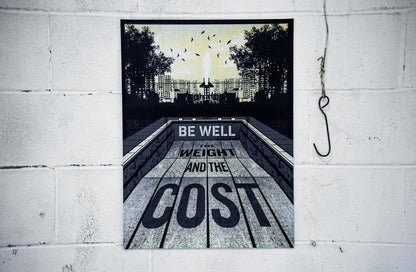 An 18x24 screen printed poster from Be Well is displayed on a white brick wall, featuring BE WELL THE WEIGHT AND THE COST in an abstract urban scene with trees, buildings, and birds. A large metal hook hangs to the right.