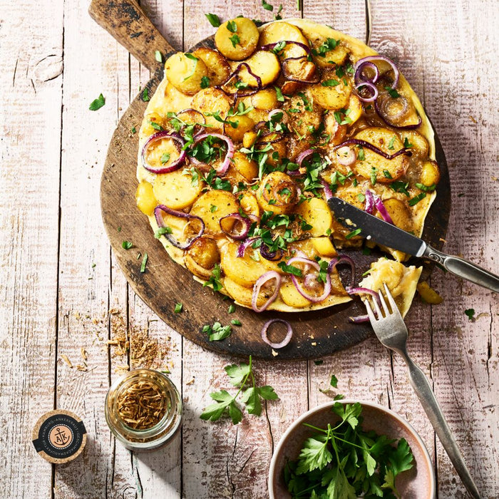 Bratkartoffelgewürz Korkenglas neben Bauernfrüstück, angerichtet auf einer Holzplatte.
