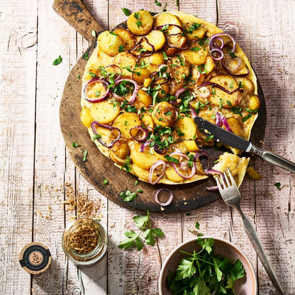 Bratkartoffelgewürz Korkenglas neben Bauernfrüstück, angerichtet auf einer Holzplatte.