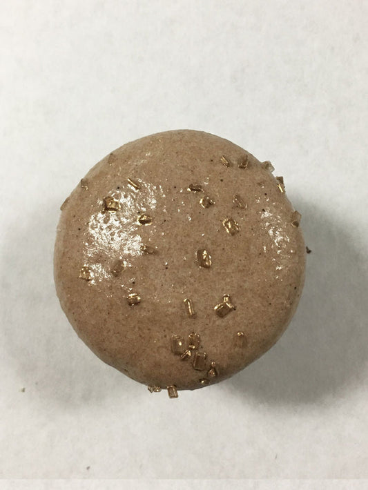 A brown chocolate macaron with gold sugar on top.