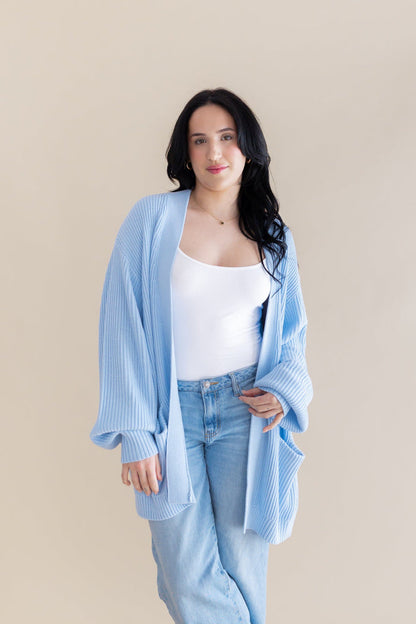 Female model posing wearing the Chunky Knit Women's Oversized Cardigan in Breeze over a white tank top and light wash jeans