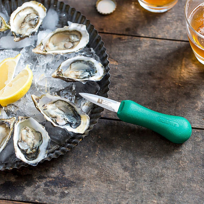 Oysters on ice with a green-handled oyster knife on a wooden surface.