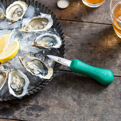 Oysters on ice with a green-handled oyster knife on a wooden surface.