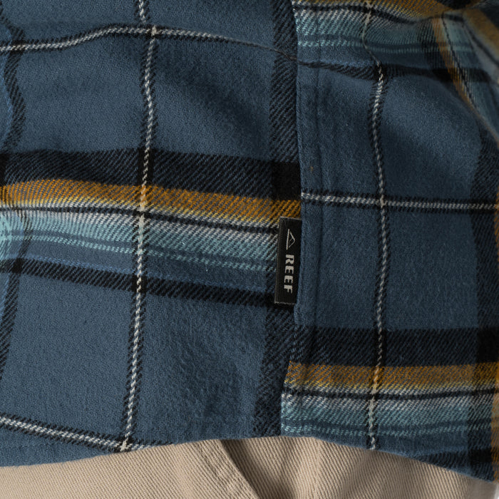 Close-up of the middle section of the blue and yellow plaid Dyson Flannel Shirt with a REEF tag visible on the side seam.