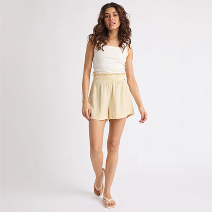 Woman wearing beige Ellie Short walking forward, paired with white sandals facing forward, showcasing beach-inspired comfort.