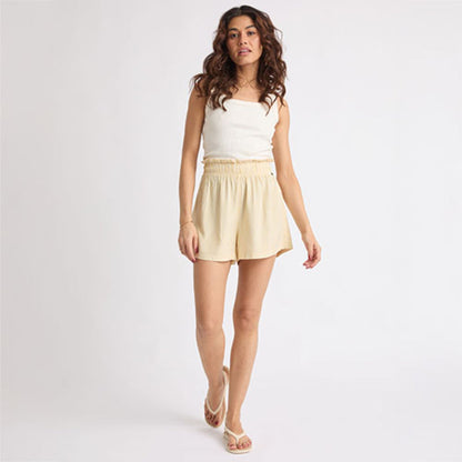 Woman wearing beige Ellie Short walking forward, paired with white sandals facing forward, showcasing beach-inspired comfort.