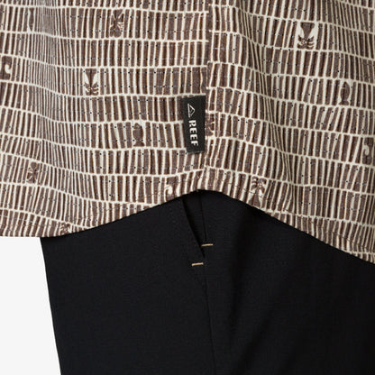 Close-up of the hem of the Ferris Classic Shirt showing surf-inspired brown pattern and REEF tag over black fabric.
