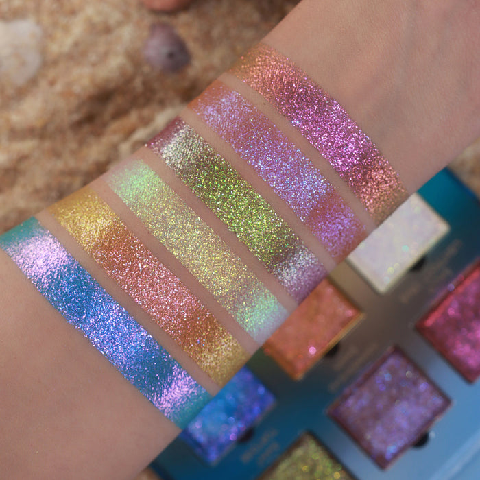 Arm swatches of all six Galápagos Palette shadows on fair skin tone. Open palette and sandy beach in the background.