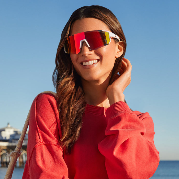 lifestyle - female at the beach wearing diff sport heat shield sunglasses with a matte white frame and sunset mirror polarized lenses front view