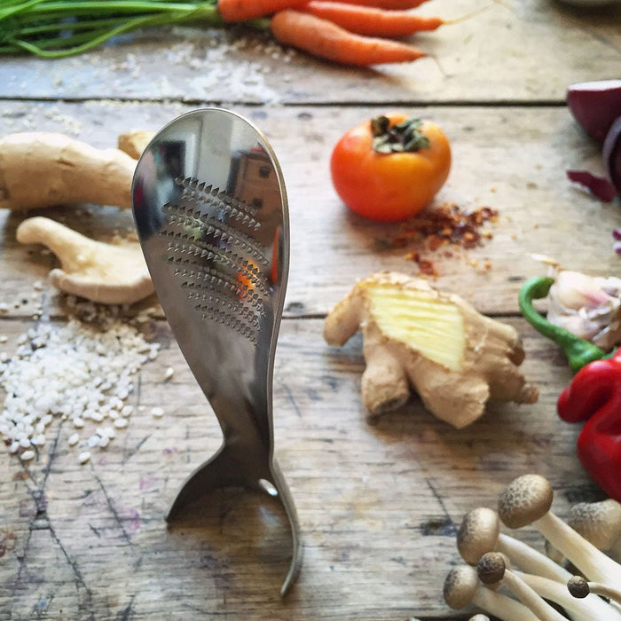 Metallic kitchen grater on a wooden surface with vegetables and spices