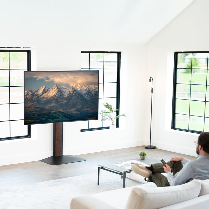 Person sitting on a couch in a modern living room with a large TV displaying mountains.