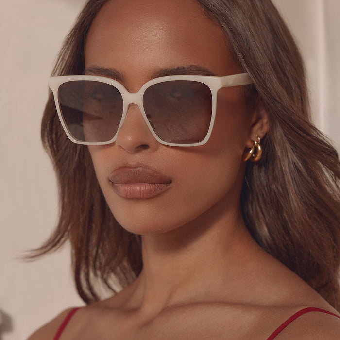 lifestyle - female at a resort wearing iconica diff eyewear naomi square oversized sunglasses with a meringue cream colored acetate frame and brown gradient polarized lenses front view