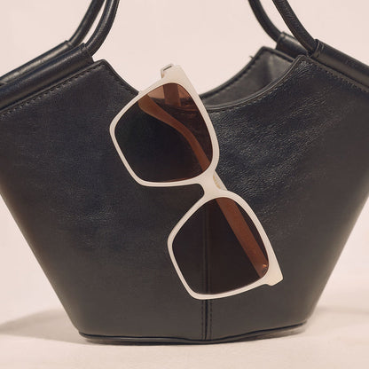 still life - iconica diff eyewear naomi square oversized sunglasses with a meringue cream colored acetate frame and brown gradient polarized lenses resting on a purse