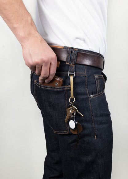Man in jeans and white shirt holds phone in pocket, keys with leather fob hang from belt loop.