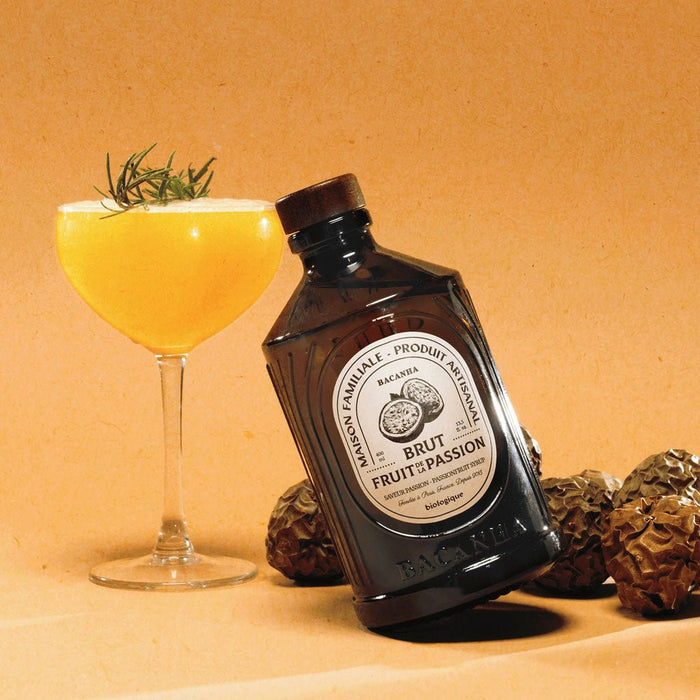 Bottle of passionfruit syrup with a cocktail and dried fruits on an orange background
