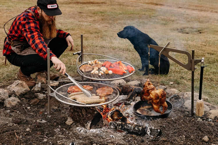 An image of a man grilling on two Outpost Grills and an Outpost Kettle Hook