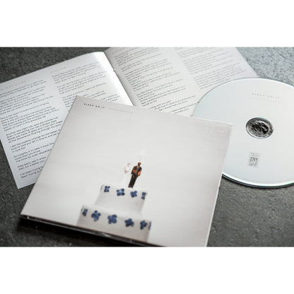 CD with artwork of a weeding cage where the bride and the groom on top of the cake are on fire. The CD itself and the Book with lyrics information are laying beside the case.
