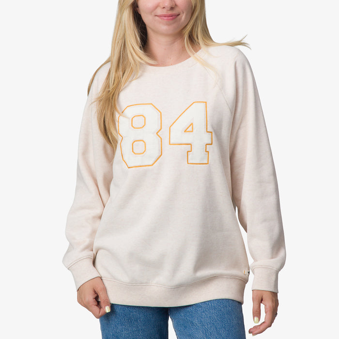 Woman wearing Oversized Raglan Fleece in oatmeal heather with orange 84 print, front view, surf-inspired comfort apparel.