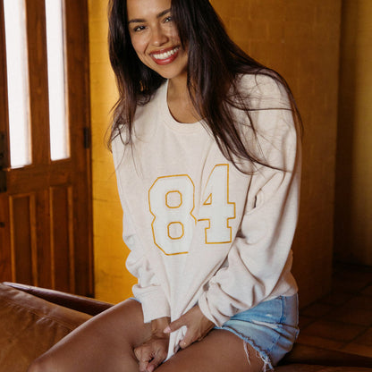 Woman wearing Oversized Raglan Fleece in oatmeal heather, sitting indoors smiling, front view showing fleece details.