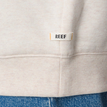 Close-up of the bottom hem on the Oversized Raglan Fleece in oatmeal heather, showing soft fabric and REEF label.