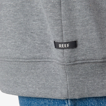 Close-up of the REEF tag on the gray hem of the Oversized Raglan Fleece for women, highlighting durable fabric.