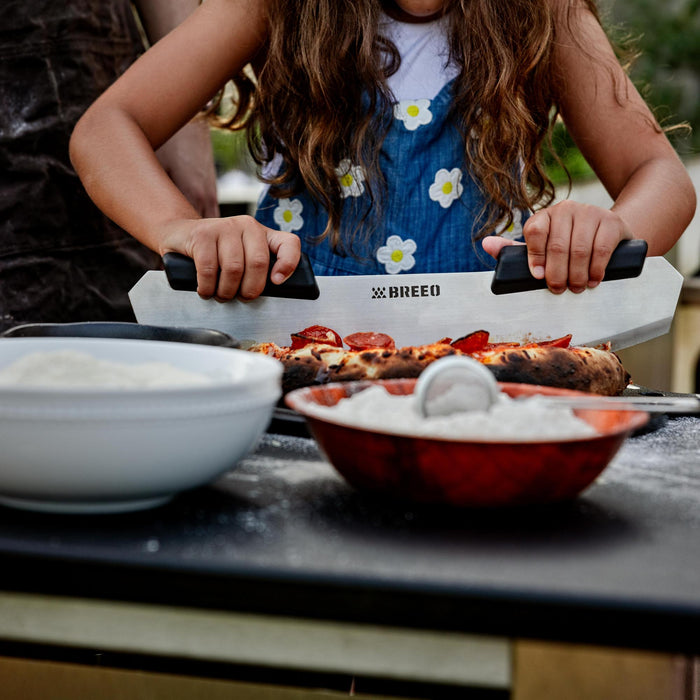 This is an image of a girl using the Breeo Pizza Rocker to slice Pizza