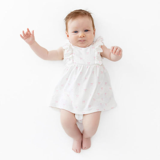 Baby in a white dress with pink bow pattern and ruffles on a white background