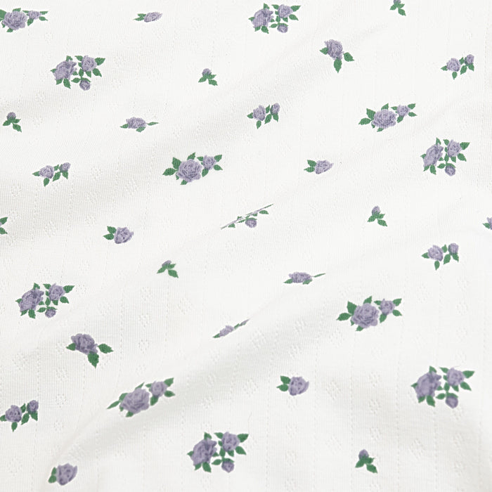 Close up of the pointelle fabric: An all-over print featuring clusters of three purple spray roses with green leaves over a white background.