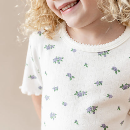 Child wearing a white shirt with purple floral patterns on a plain background