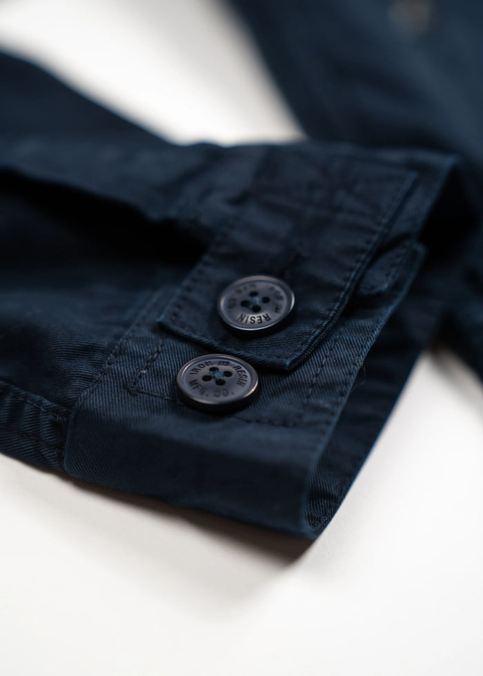 Close-up of a navy blue shirt sleeve with two dark buttons on a white background, highlighting detailed stitching.