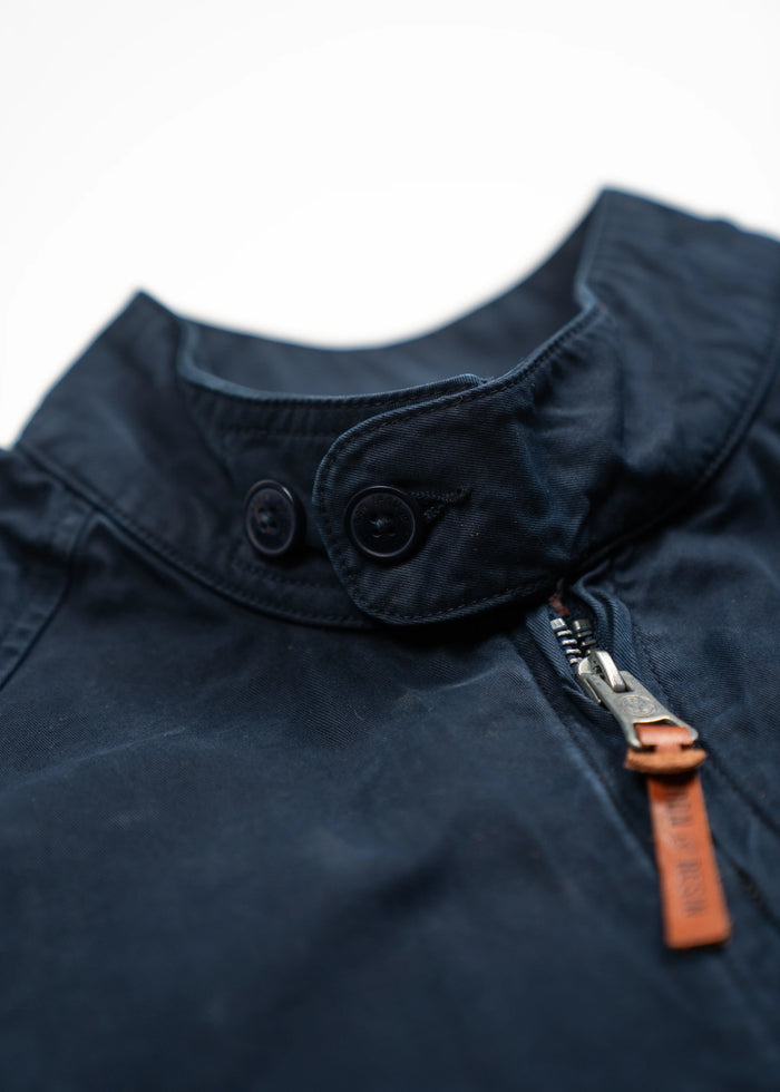 Close-up of a navy jacket collar with buttons and a zipper featuring a brown leather pull tab, highlighting its stylish design.