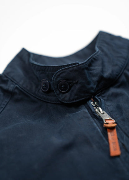 Close-up of a navy jacket collar with buttons and a zipper featuring a brown leather pull tab, highlighting its stylish design.