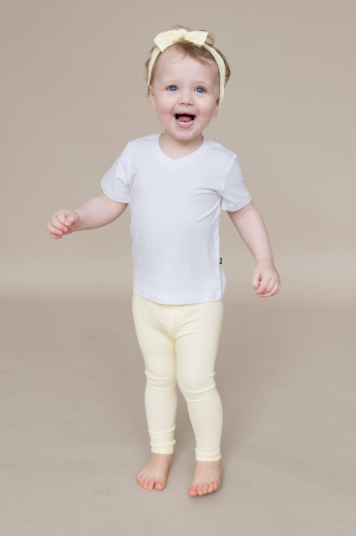 Smiling toddler wearing the Ribbed Leggings in Chamomile paired with a white v-neck