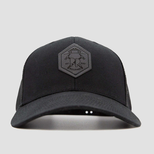 Front view of a black baseball cap with a hexagonal patch on the front, featuring a logo with two crossed hammers and text that reads EST 2007 and BUILDINGS on a plain light gray background.