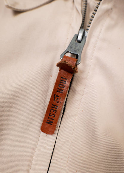 Close-up of a beige jacket zipper with a brown leather pull tab labeled "Iron and Resin," highlighting the brand detail.
