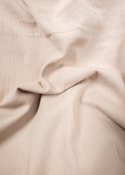 Cream herringbone fabric with soft folds, creating a textured, elegant pattern. The light enhances its subtle, intricate design.