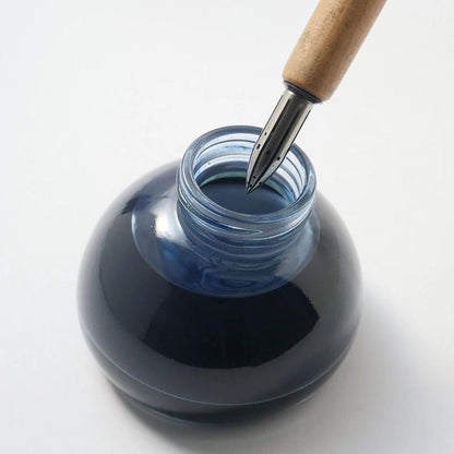 Dip pen above blue bottle of ink on light surface