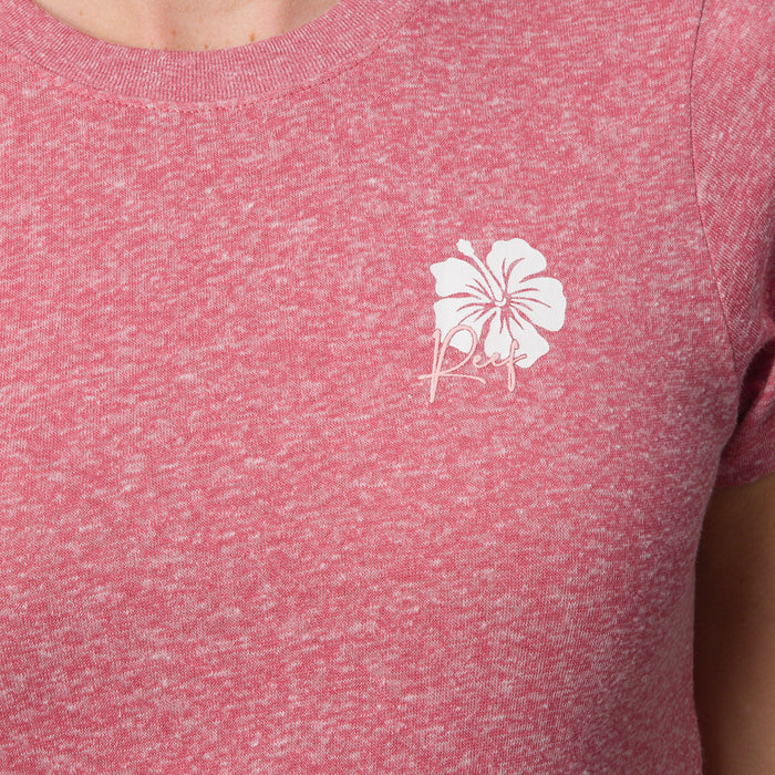 Close-up of a woman's upper torso wearing the mauve Saylor Fitted Tee with a white hibiscus logo, beach-inspired comfort apparel.
