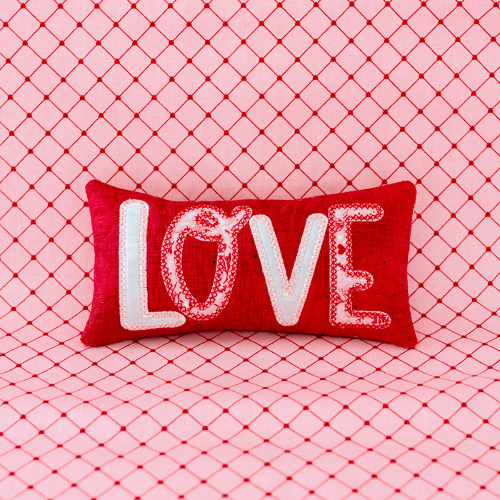 Red pillow with 'LOVE' text on a pink textured background