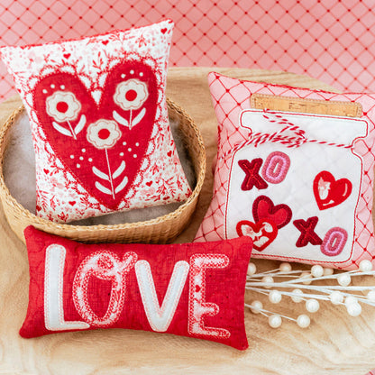 Three decorative pillows with heart and 'LOVE' designs on a red checkered background.