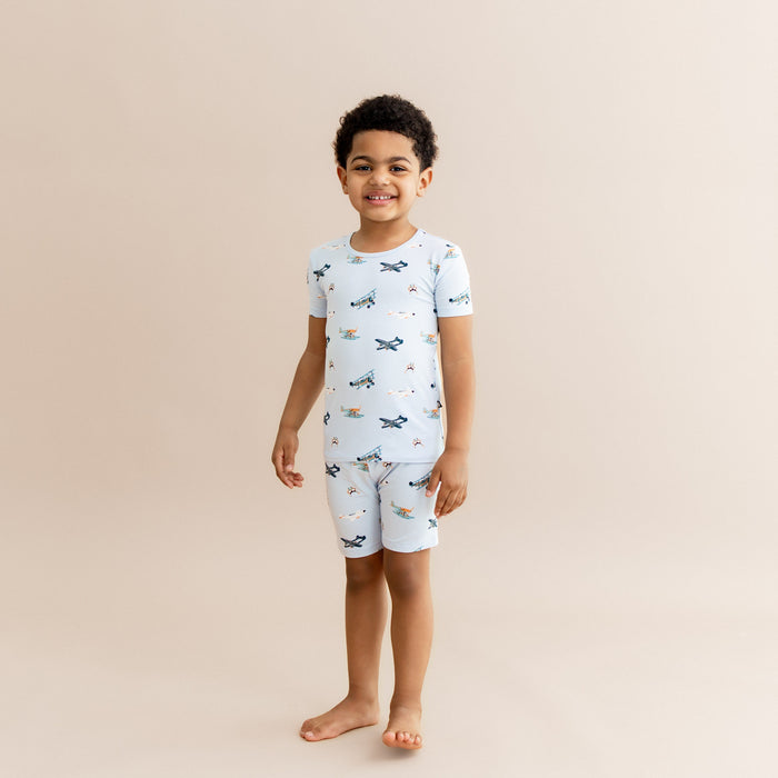 Smiling boy wearing the Short Sleeve Pajamas in Take Off standing in front of a light taupe background
