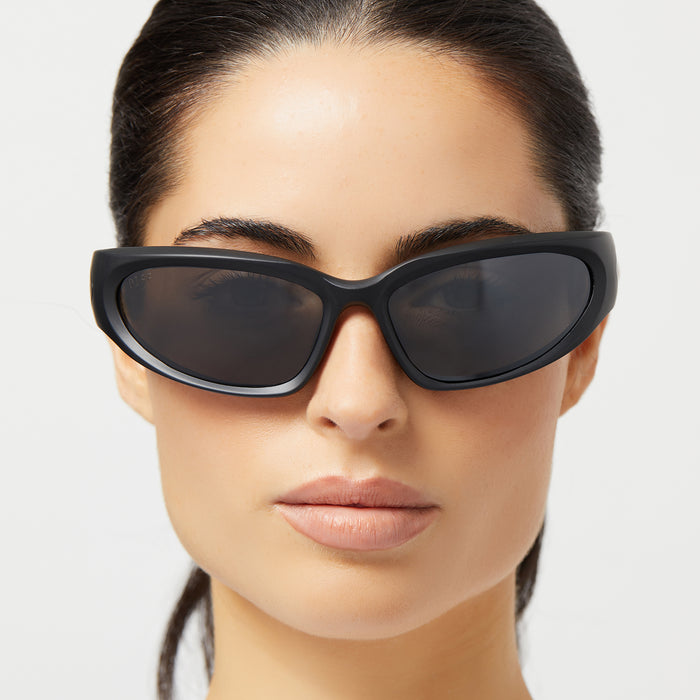 on model - female wearing diff sport side out wrap sunglasses with a matte black frame and grey with silver flash polarized lenses front view