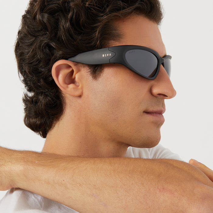 on model - male wearing diff sport side out wrap sunglasses with a matte black frame and grey with silver flash polarized lenses