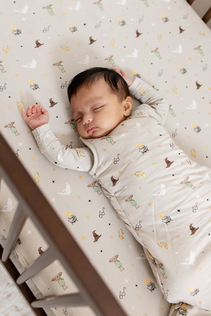 Baby wearing a beige Harry Potter patterned sleep bag sleeping on a similar print crib sheet.