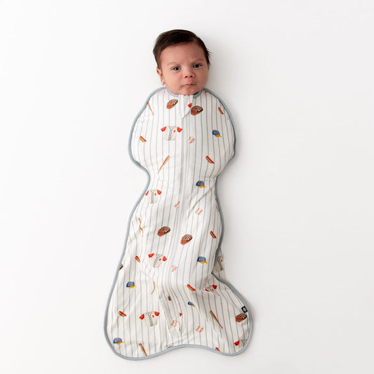 Newborn laying on a white surface wearing the Swaddle Bag in Home Run 0.5