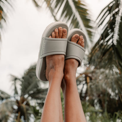 Sydnee Cutback Low - Sage - on a pair of feet up in the air with palm trees in the background